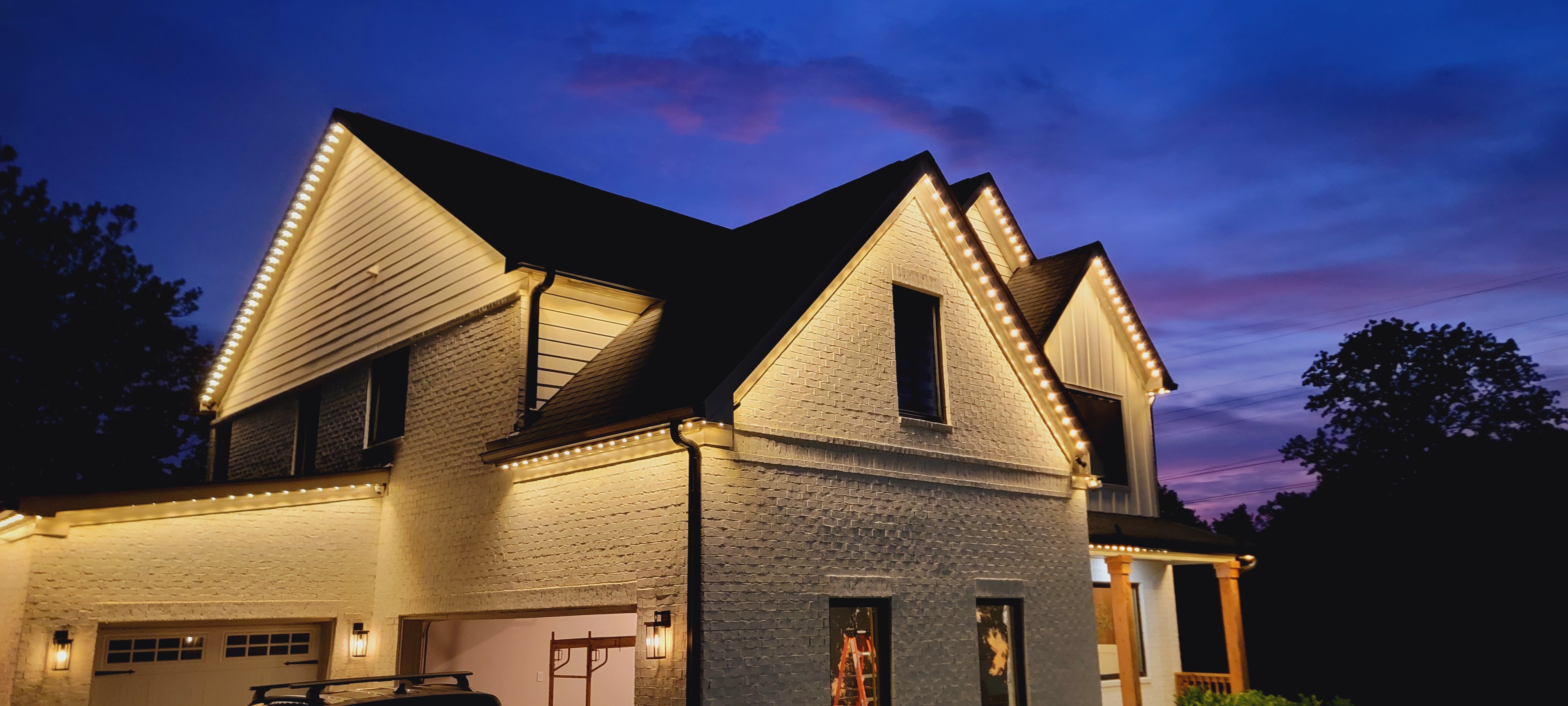 Two story home at dusk with warm permanent LED lighting on rooflines and gables.